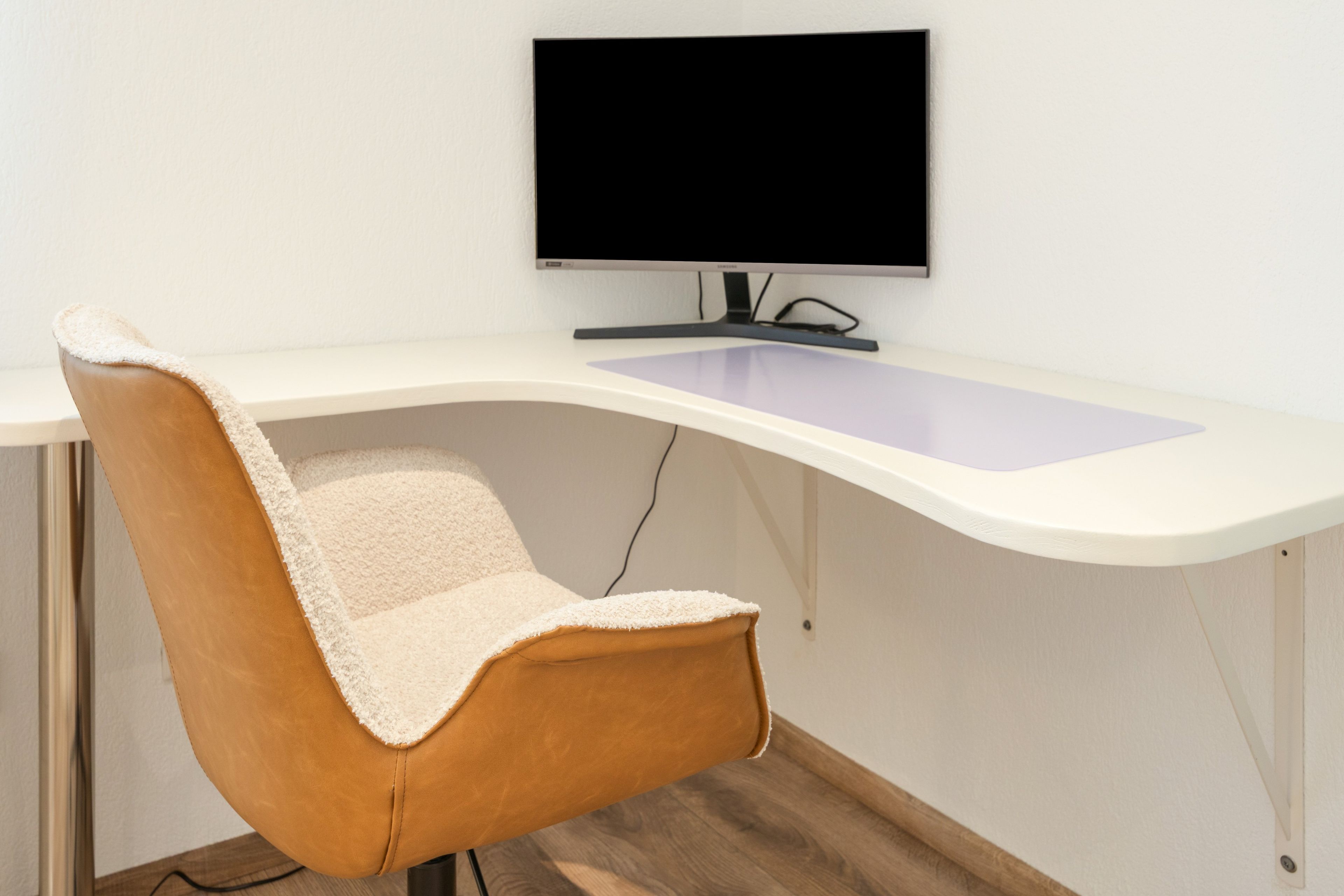 Un fauteuil de bureau moderne, doté d’un haut dossier et d’un coussin, placé devant un bureau blanc sur lequel se trouve un écran plat.