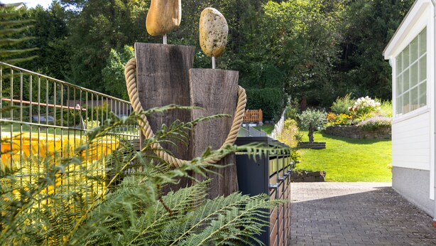 En have med en træskulptur, et metalsplejl og en bygning i baggrunden.