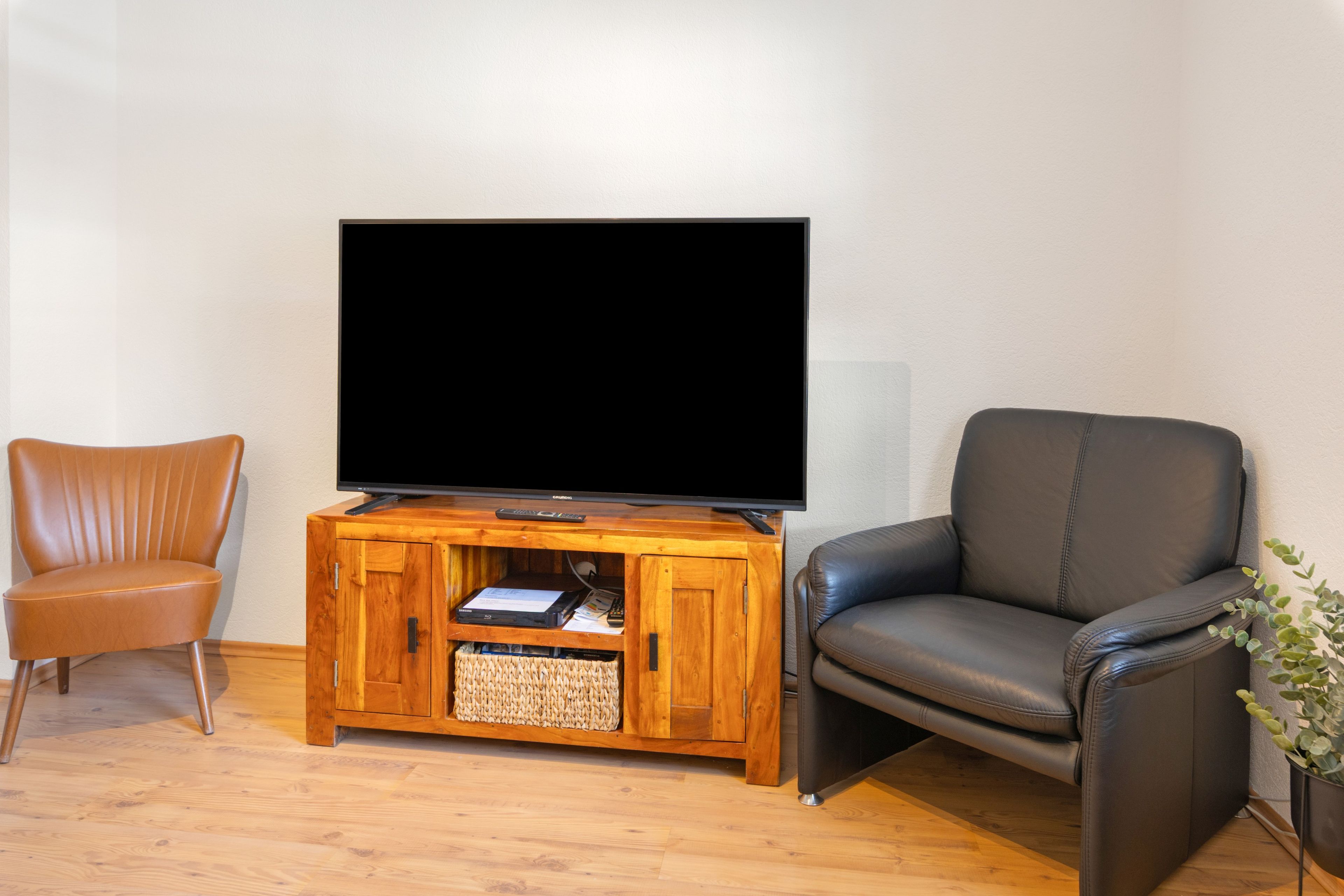 Una sala de estar con un mueble de madera para entretenimiento, un televisor, un sillón de cuero y una silla marrón.