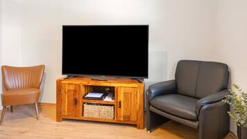 A living room with a wooden entertainment unit, a television, a leather armchair, and a brown chair.