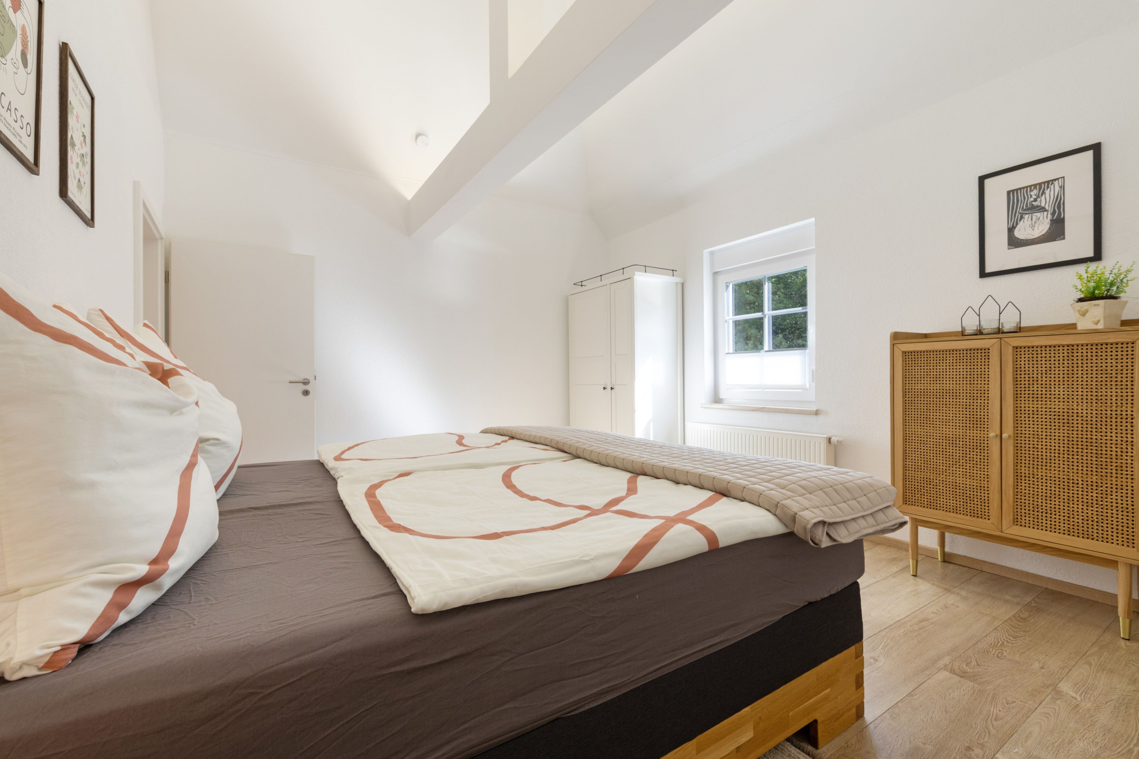 A bedroom with a bed, a wardrobe, a window, and a ceiling with beams.