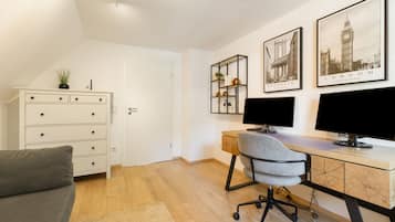 A modern office space with a desk, two monitors, a chair, a white dresser, and framed cityscape pictures on the wall.