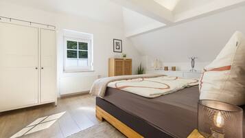 A bedroom with a bed, a window, a radiator, a wardrobe, and a bedside table with a lamp.