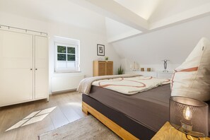 A bedroom with a bed, a window, a radiator, a wardrobe, and a bedside table with a lamp. - Apartment “Welcome” with Private Rooftop Terrace (Olpe)