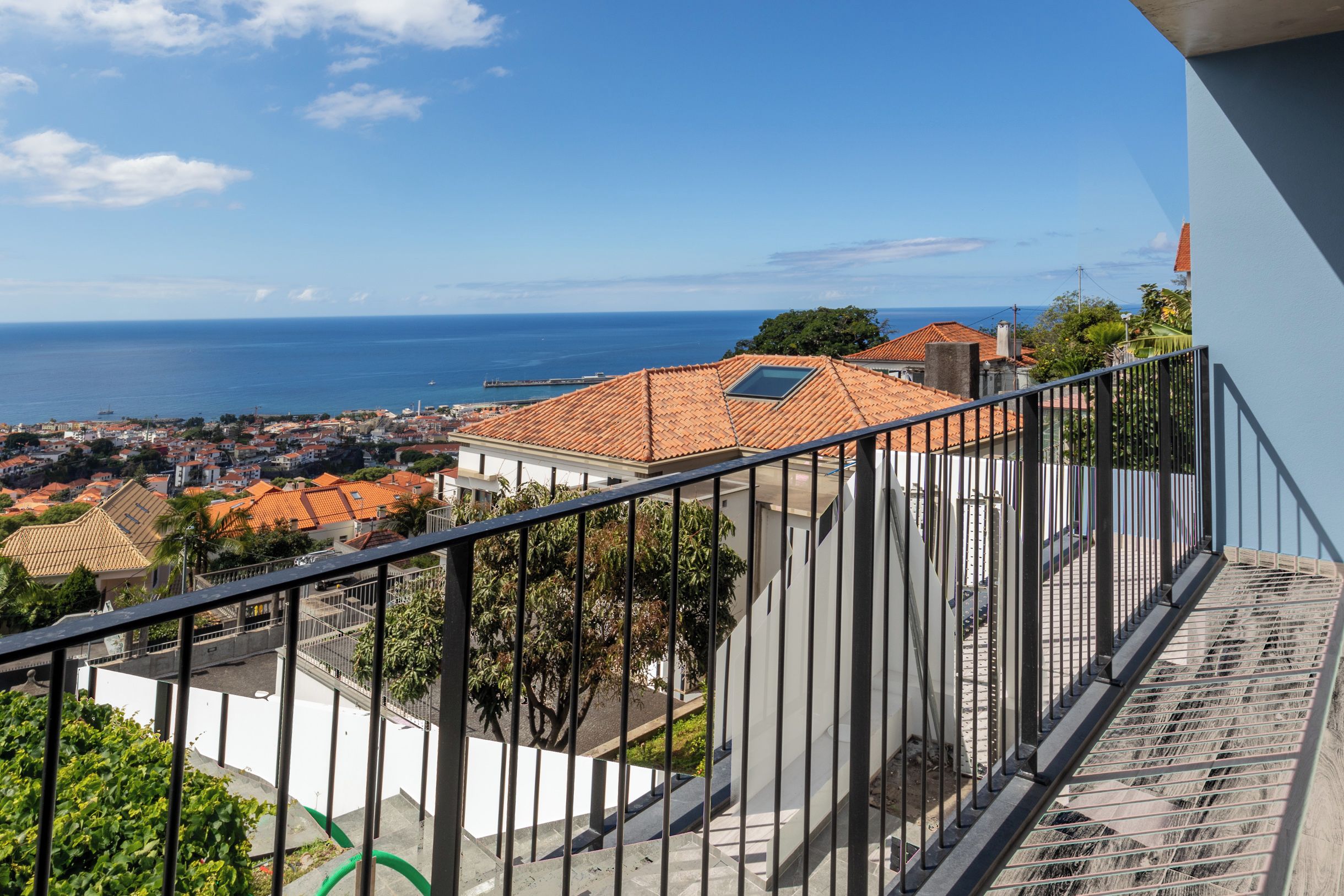 Un balcone con vista su una cittadina costiera, cielo sereno e mare in lontananza.
