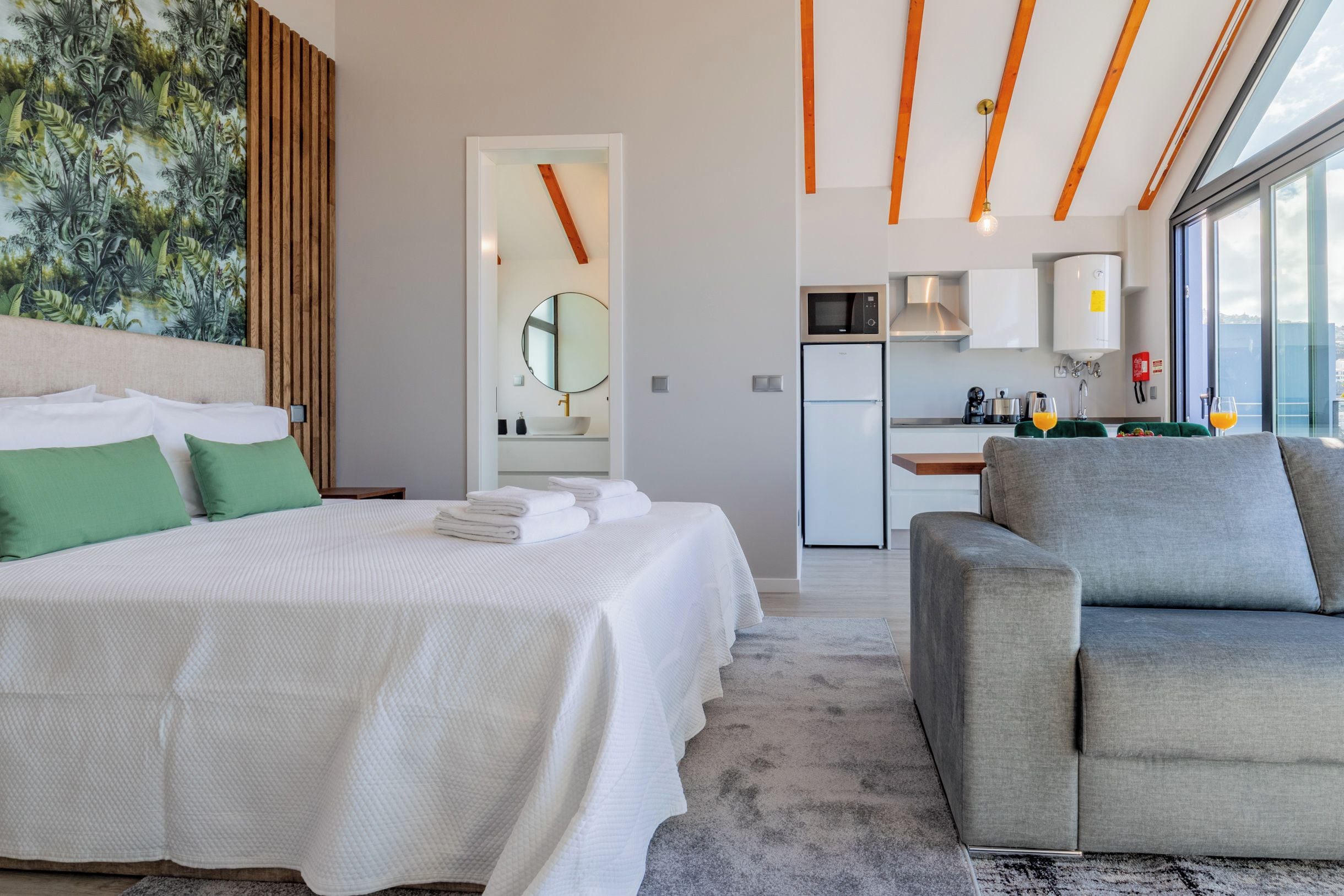 Une chambre d’hôtel moderne équipée d’un lit, d’un coin salon, d’une cuisine et d’une grande fenêtre.