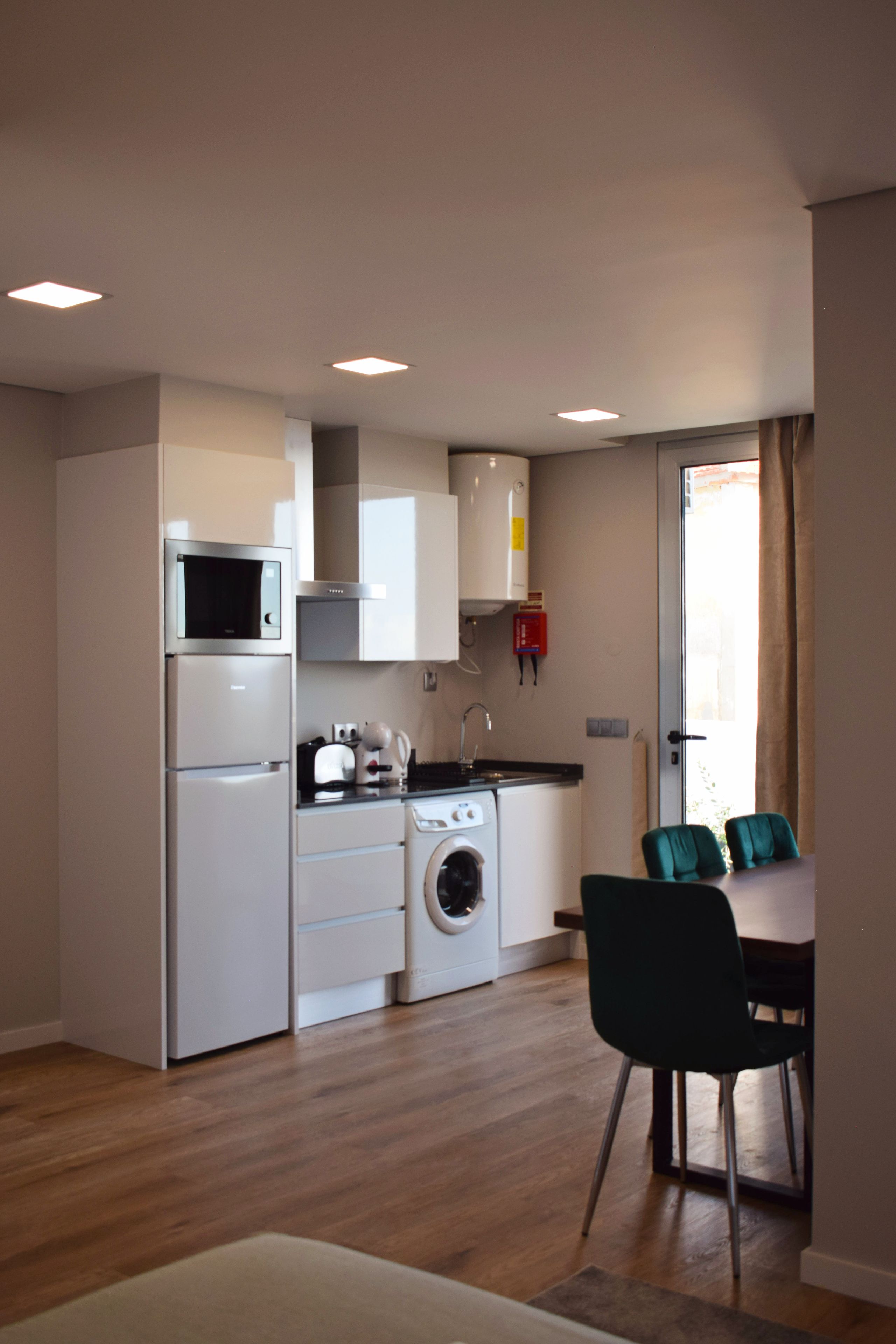 Een compacte keuken met een magnetron, oven en wasmachine. Er is een eethoek met een tafel en stoelen.
