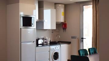 Een compacte keuken met een magnetron, oven en wasmachine. Er is een eethoek met een tafel en stoelen.