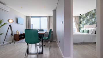 A modern hotel room with a balcony, a dining area, and a bed with a view.