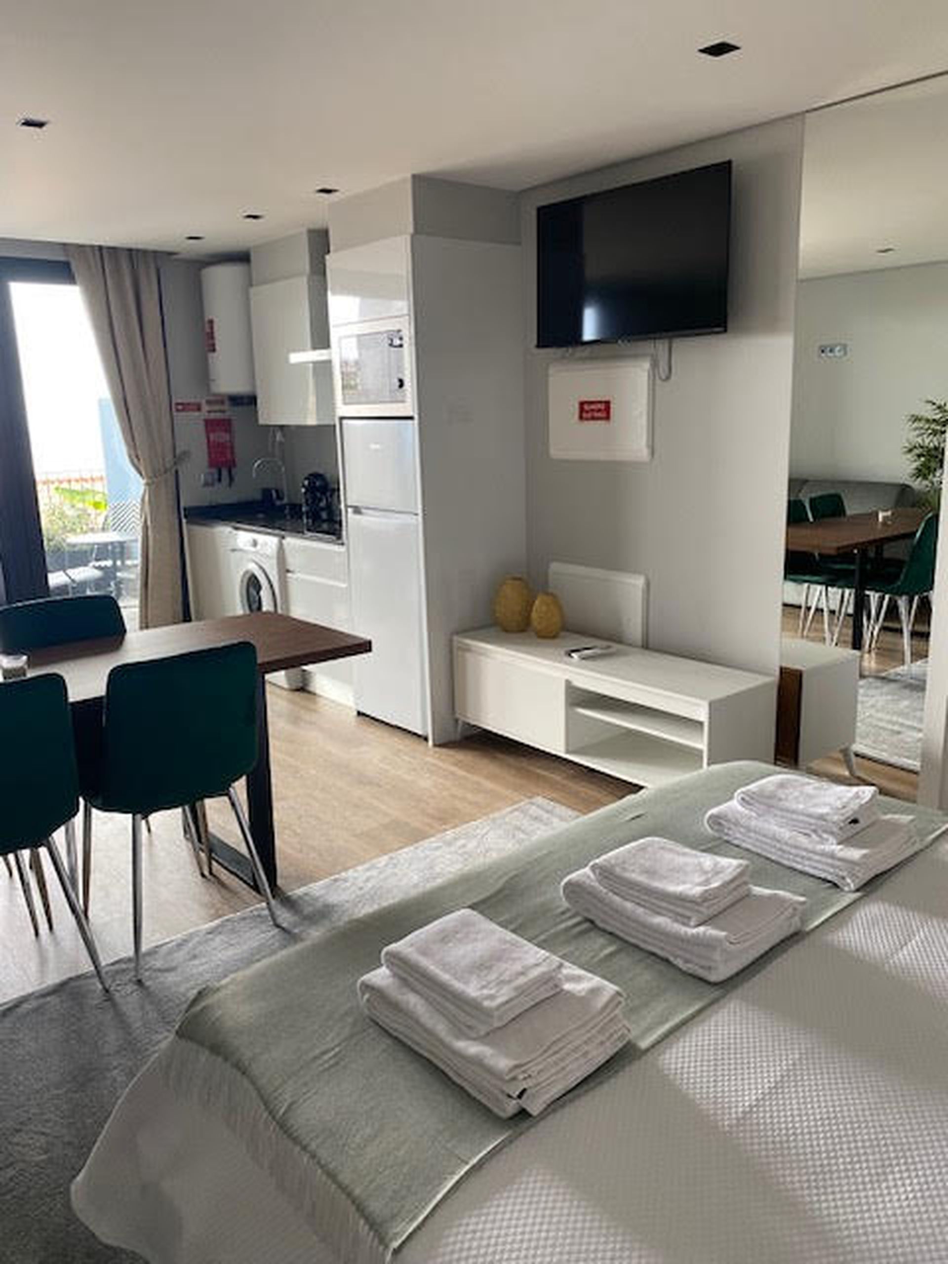 Een moderne hotelkamer met een bed, bureau, stoel, flatscreen televisie, een klein keukenhoekje en uitzicht naar buiten.