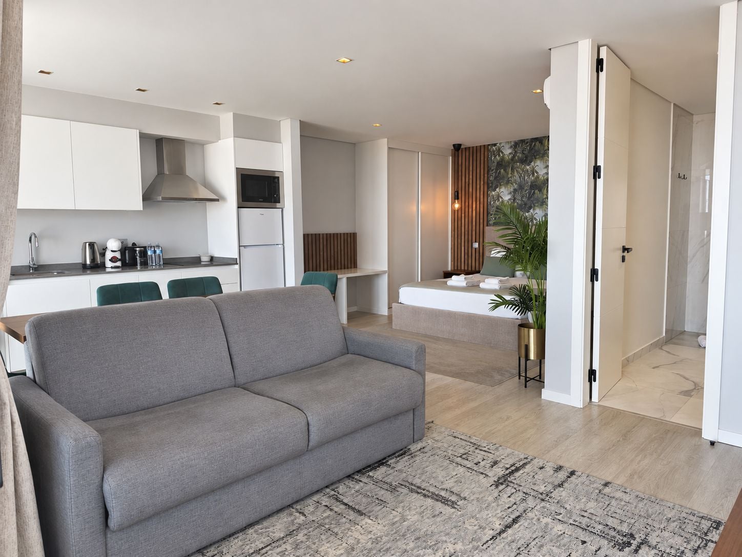 Una sala de estar moderna con un sofá gris, una zona de cocina con armarios blancos y un comedor con sillas verdes.