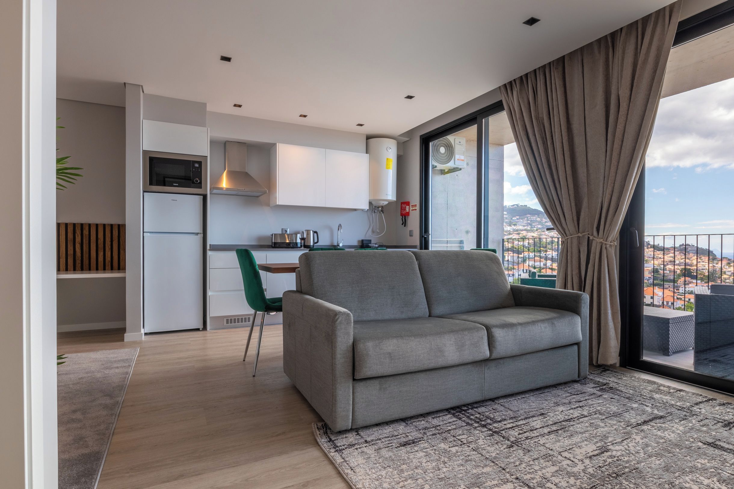 Een modern appartement met een grijze bank, een eethoek en een keuken.