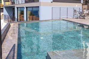 Une piscine aux eaux cristallines, bordée de pierres, entourée d’un balcon doté d’une balustrade.