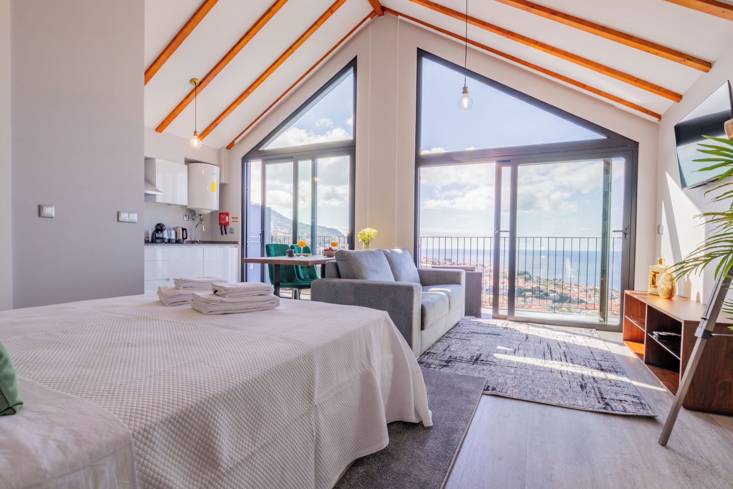 Un dormitorio moderno con una cama grande, una zona de estar, un balcón con vistas y un televisor en la pared.
