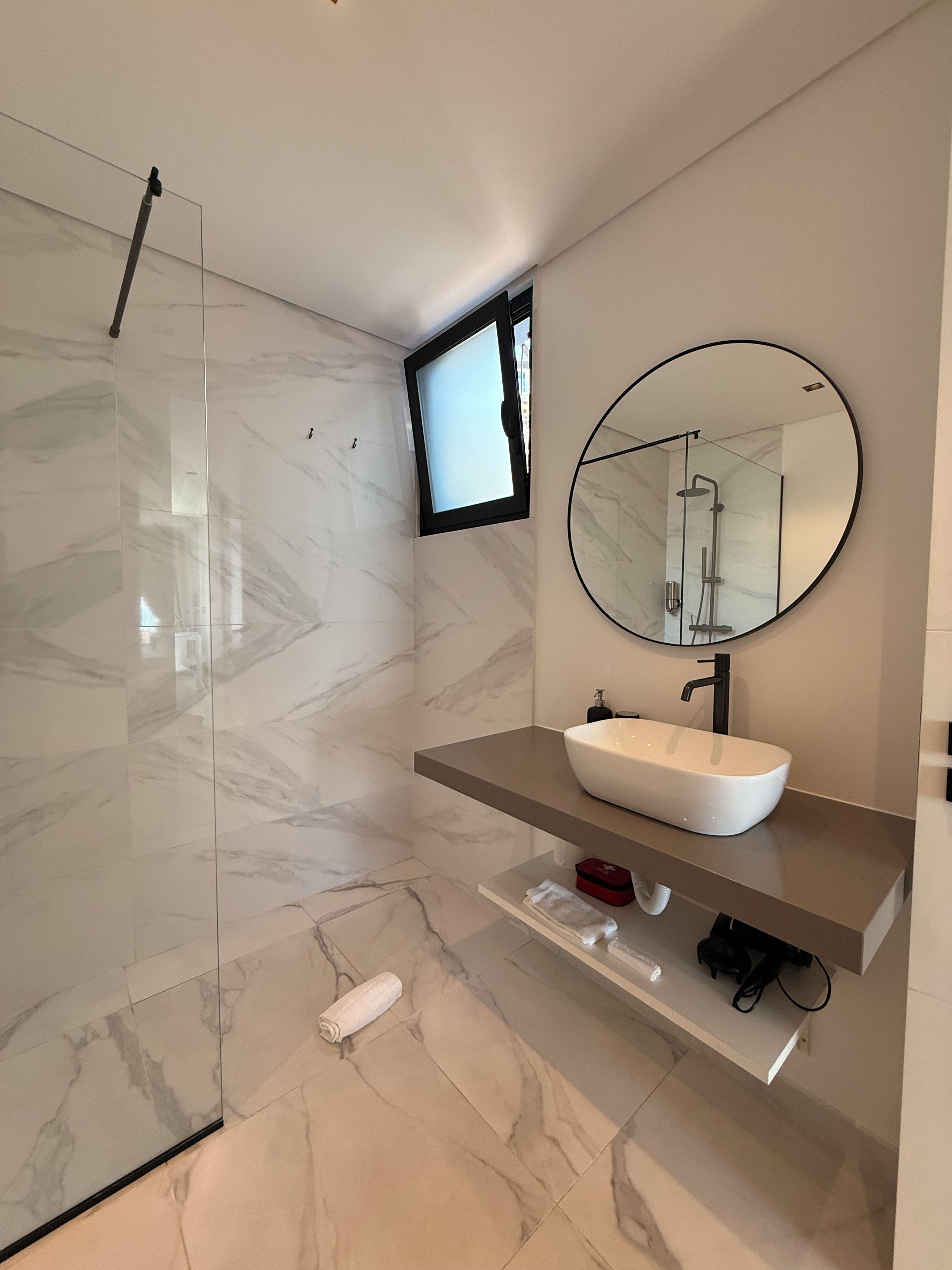 Un baño moderno con cabina de ducha de vidrio, un lavabo blanco y un espejo grande.