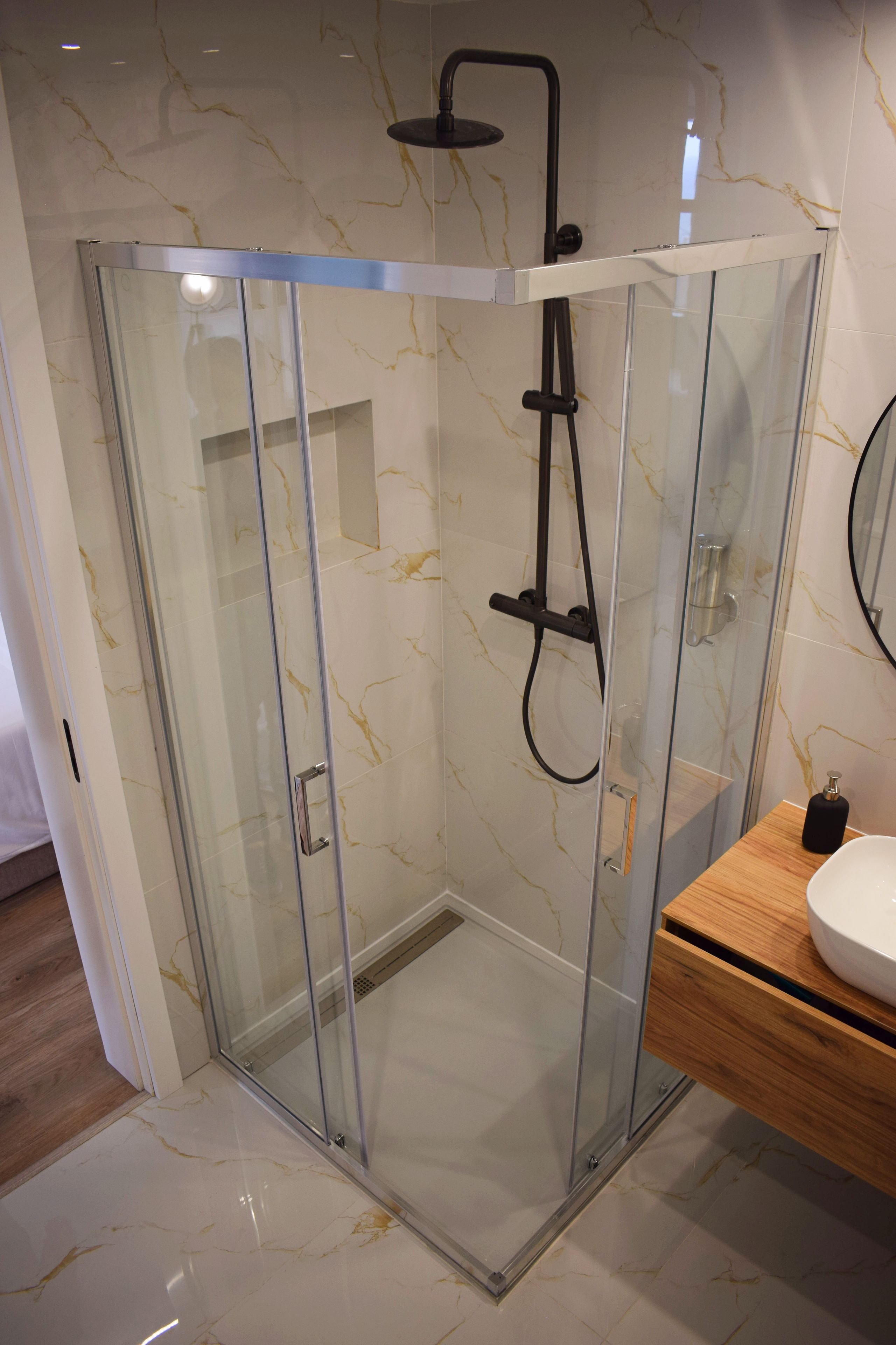 Un baño moderno con ducha envuelta en vidrio, tocador de madera y piso de baldosas de mármol.