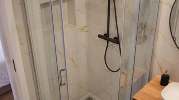 Un baño moderno con ducha envuelta en vidrio, tocador de madera y piso de baldosas de mármol.