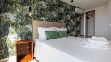 A hotel room with a bed, a nightstand, a wooden side table, a wardrobe, and a wall with a tropical leaf pattern.