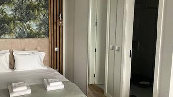 A hotel room with a bed, a green chair, a wardrobe, and a door leading to a bathroom.