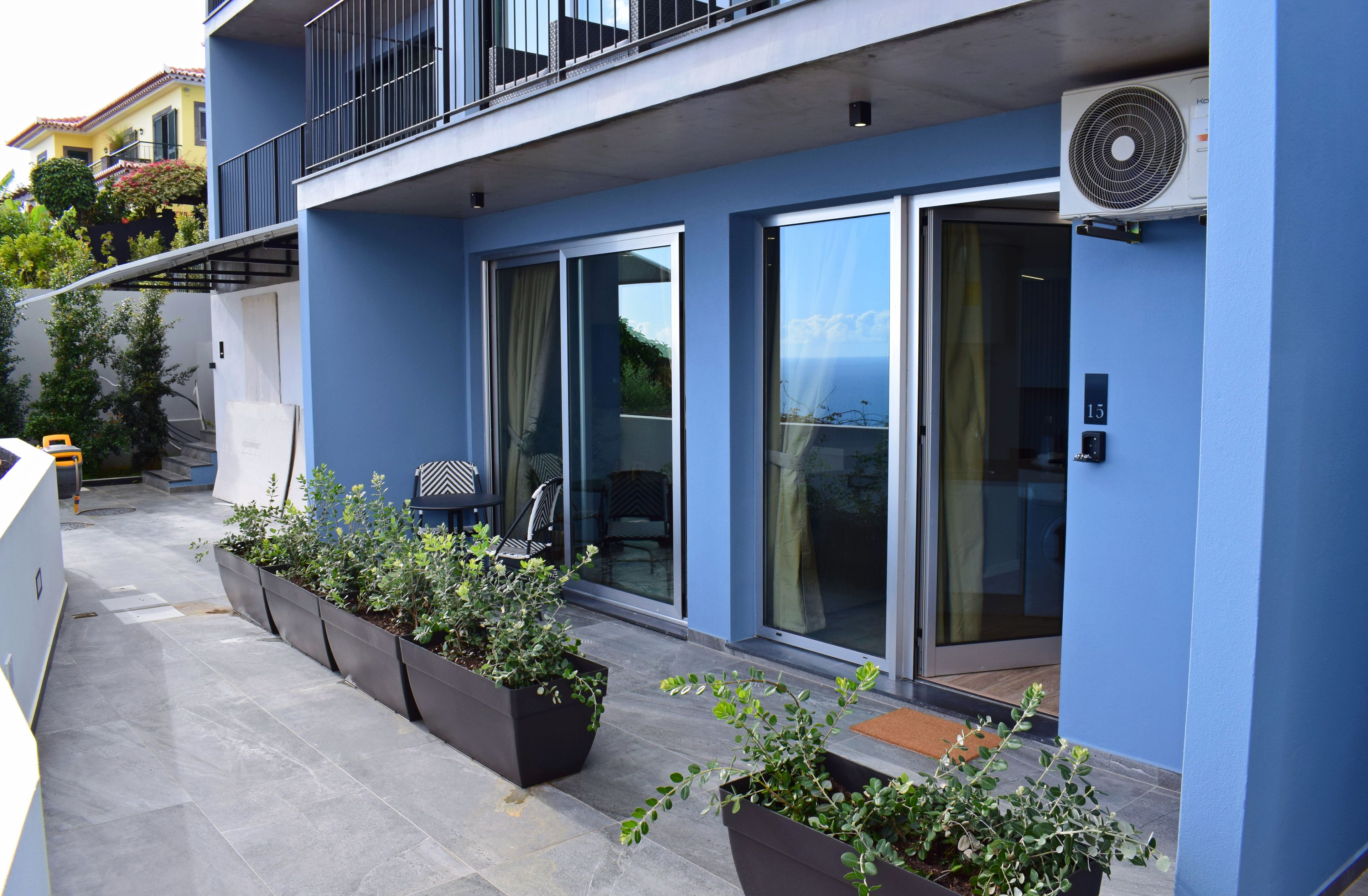 Un edificio moderno con fachada azul, puertas correderas de vidrio y un balcón con plantas en macetas.