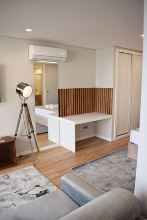 A modern, well-lit room with a wooden accent wall, a white desk, a standing lamp, and a grey sofa.