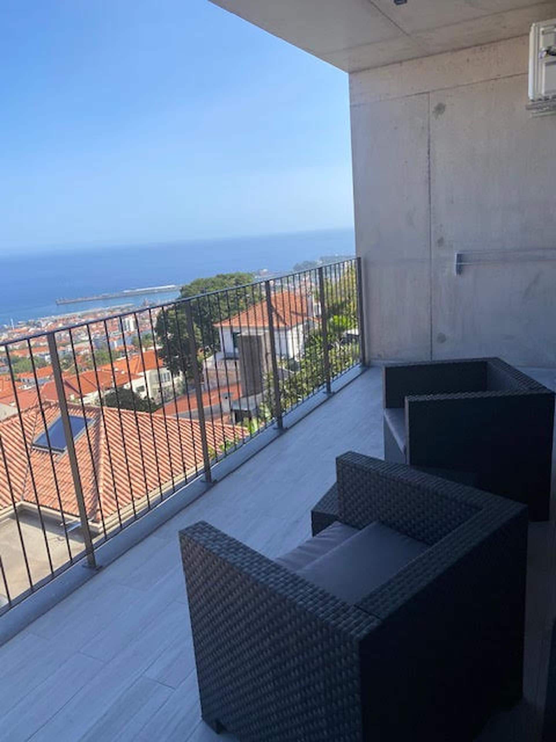 A balcony with wicker furniture and a view of the sea and buildings.
