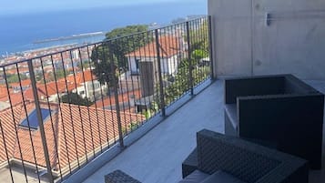 A balcony with wicker furniture and a view of the sea and buildings.