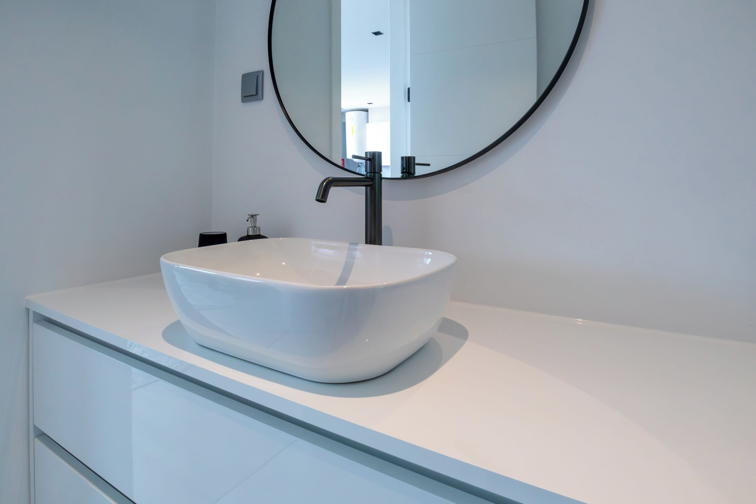 A modern bathroom with a white sink, a round mirror, and a sleek faucet.