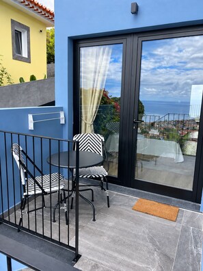 Uma varanda com mesa e cadeiras, vista para o mar e um edifício com fachada amarela.