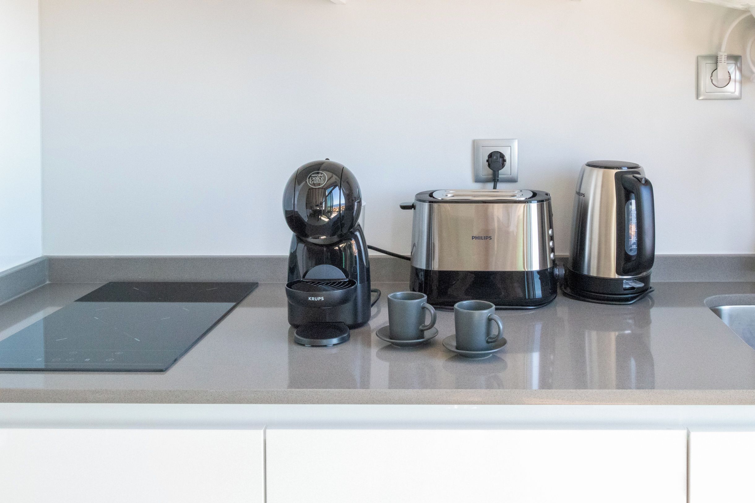 A kitchen with a coffee maker, a kettle, and two cups on the counter.
