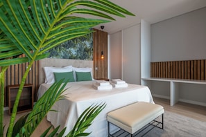 A modern bedroom with a bed, pillows, a bench, a wall-mounted shelf, and a large plant.