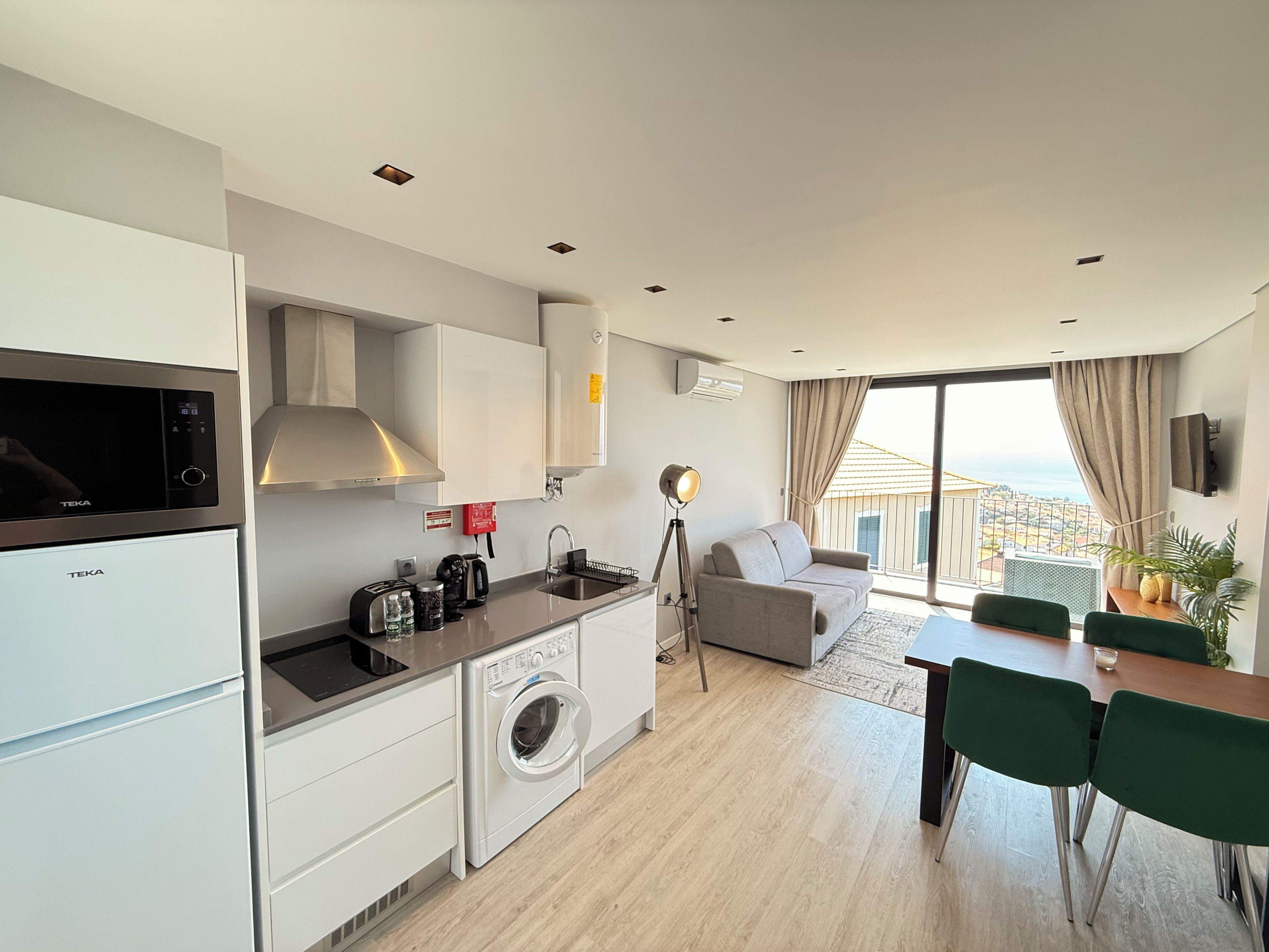 A modern kitchen with a washing machine, a dining area with a table and chairs, and a sofa.