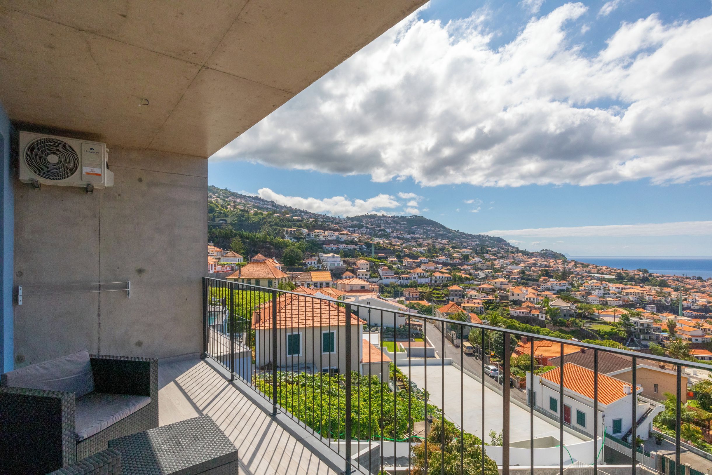 Un balcón con vistas a un pueblo costero, una estructura de concreto y un equipo de aire acondicionado.