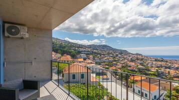 Un balcón con vistas a un pueblo costero, una estructura de concreto y un equipo de aire acondicionado.