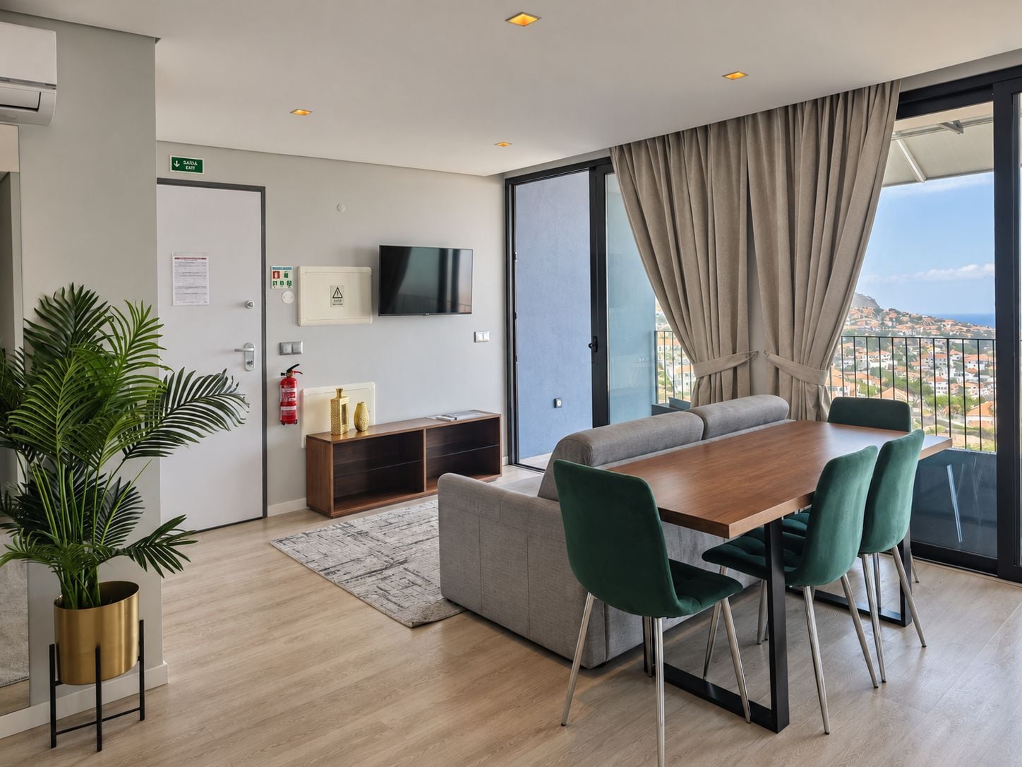 Een moderne hotelkamer met een eethoek, een flatscreen televisie, een brandblusser en uitzicht op de stad.