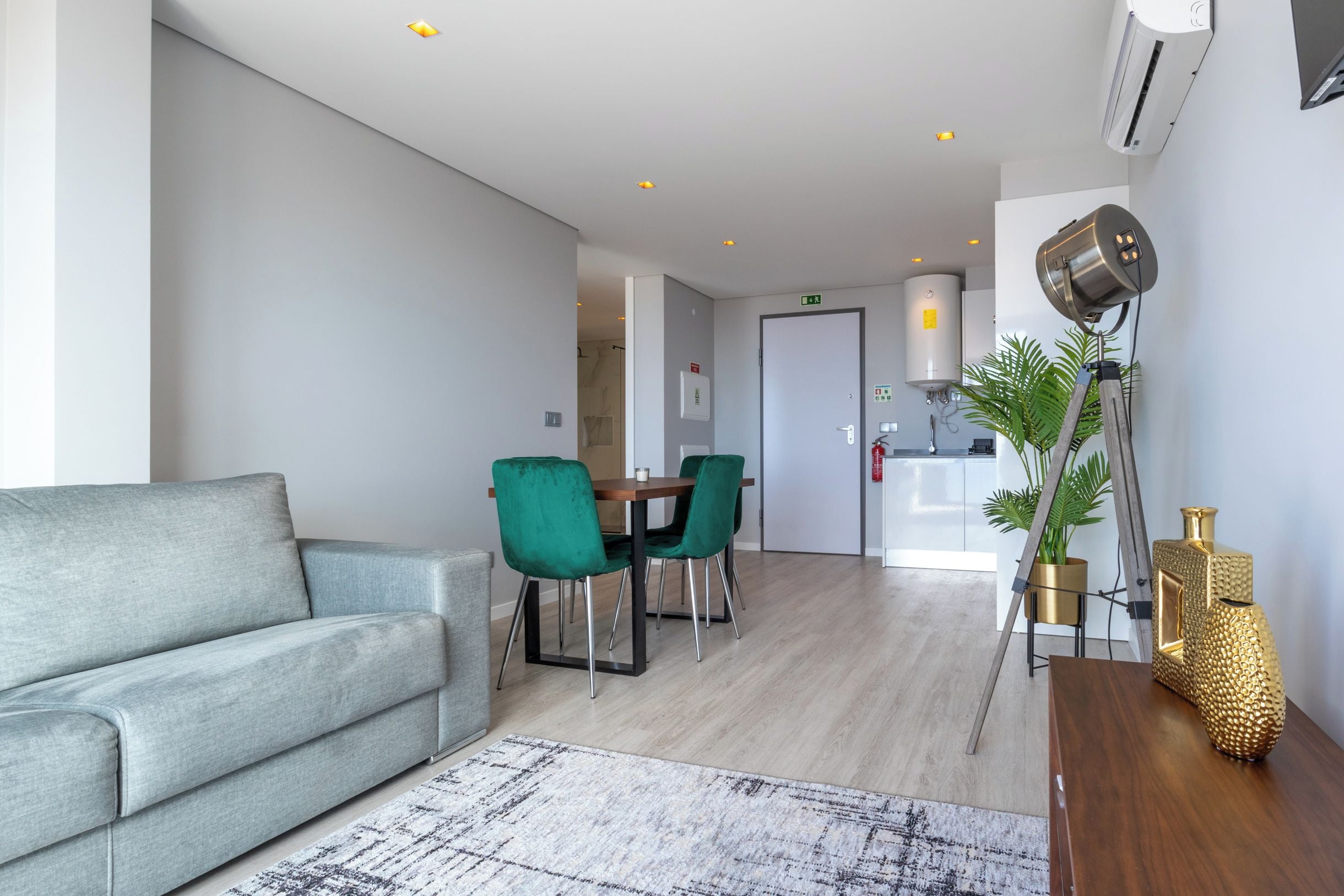 Una sala de estar moderna con un sofá gris, una zona de comedor con sillas verdes y una cocina con estufa blanca.