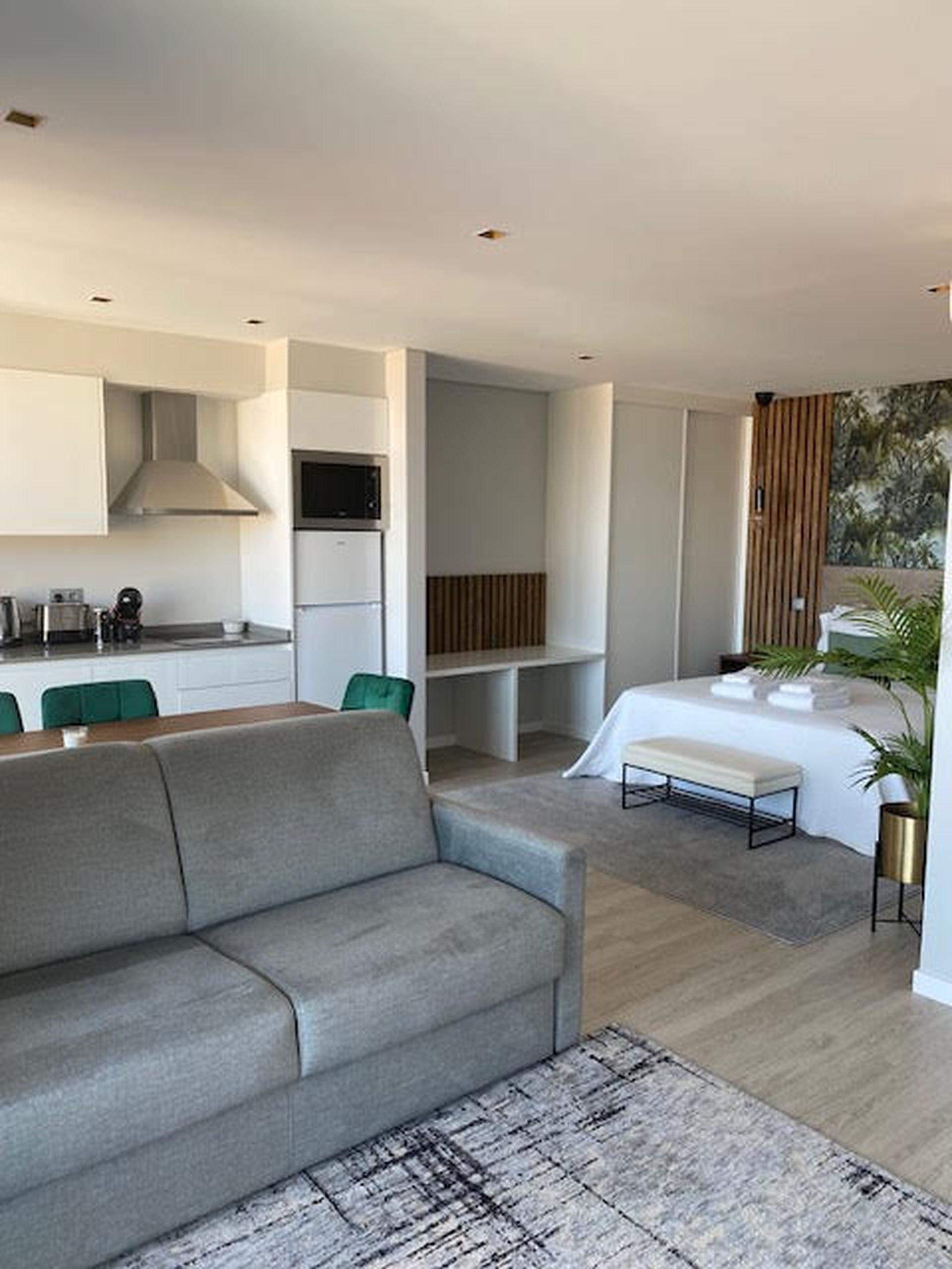Un intérieur moderne avec un canapé gris, une table à manger et un coin cuisine doté de meubles blancs et d’un four à micro-ondes.