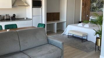 Un intérieur moderne avec un canapé gris, une table à manger et un coin cuisine doté de meubles blancs et d’un four à micro-ondes.