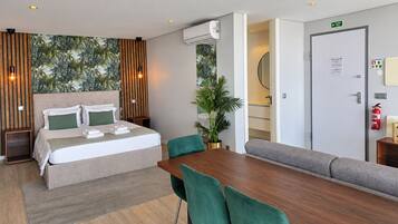 A modern hotel room with a bed, a dining table, chairs, a sofa, a potted plant, and an air conditioning unit.