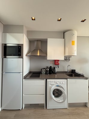 A compact kitchen with a microwave, toaster, coffee maker, sink, and a built-in washing machine.