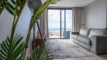 Un salón moderno con un sofá gris, un ventanal con vistas y una planta en primer plano.