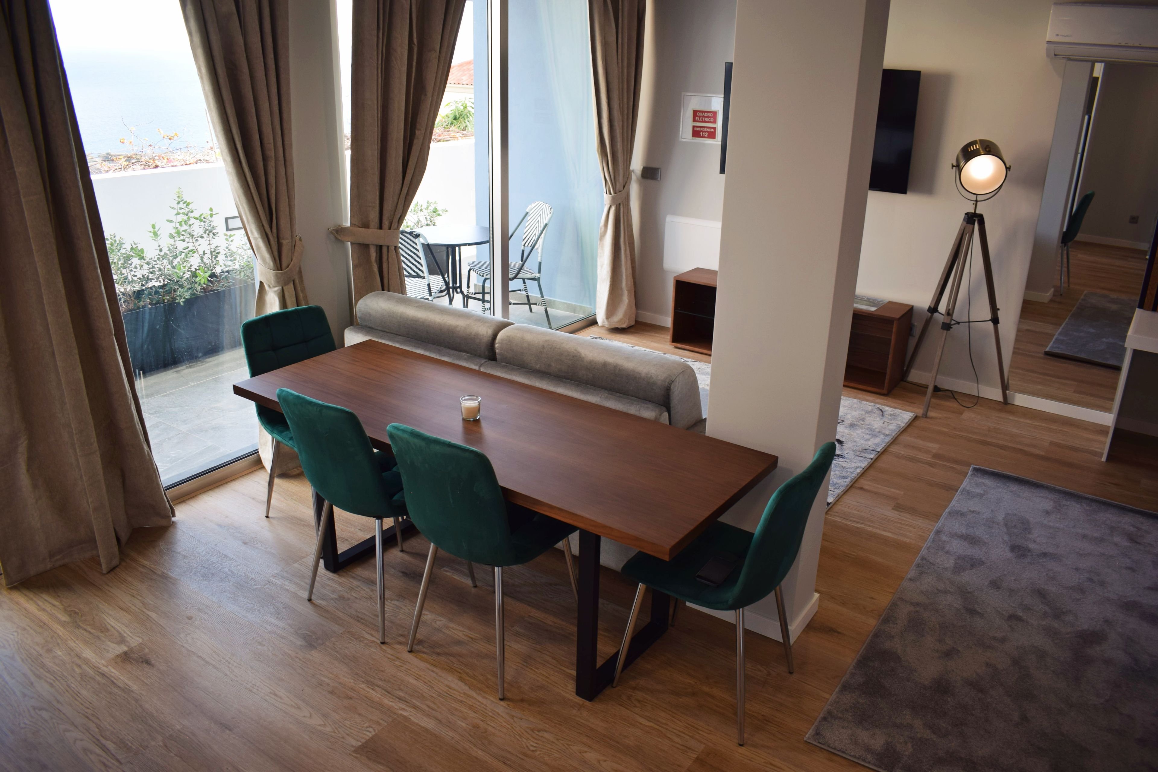 Un comedor moderno con una mesa de madera y sillas verdes, un sofá, y vistas al exterior.