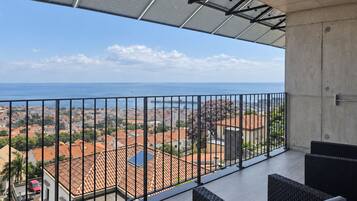 A balcony with a view of a coastal cityscape, equipped with solar panels and outdoor furniture.