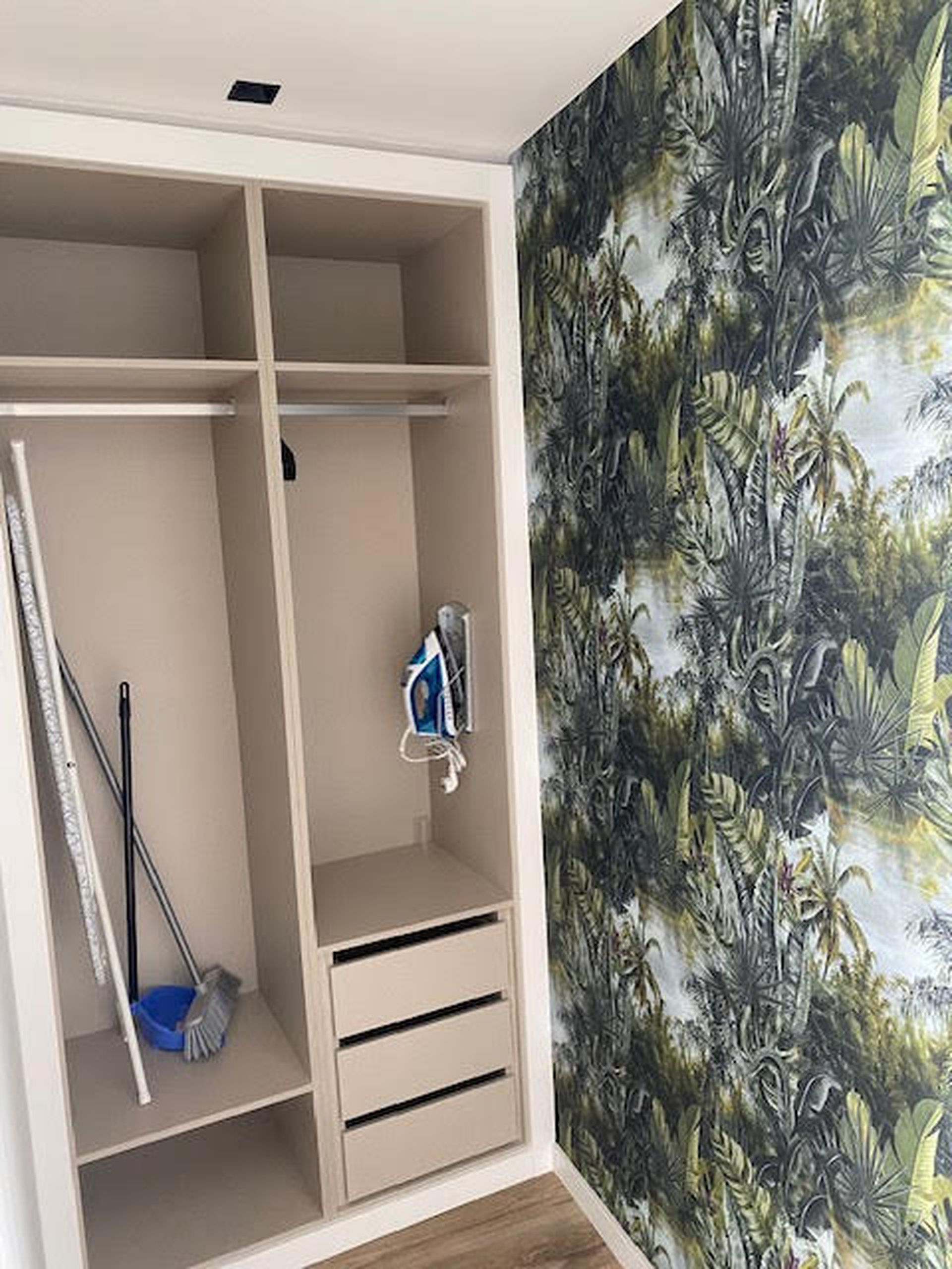 A room with a wardrobe, a mop, and a vacuum cleaner.