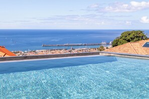 Piscina azul e límpida com vista para o mar e um cais distante.