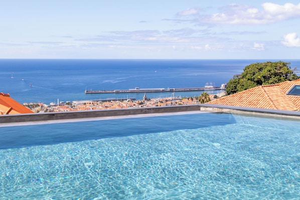 A clear blue pool with a view of the sea and a distant pier.