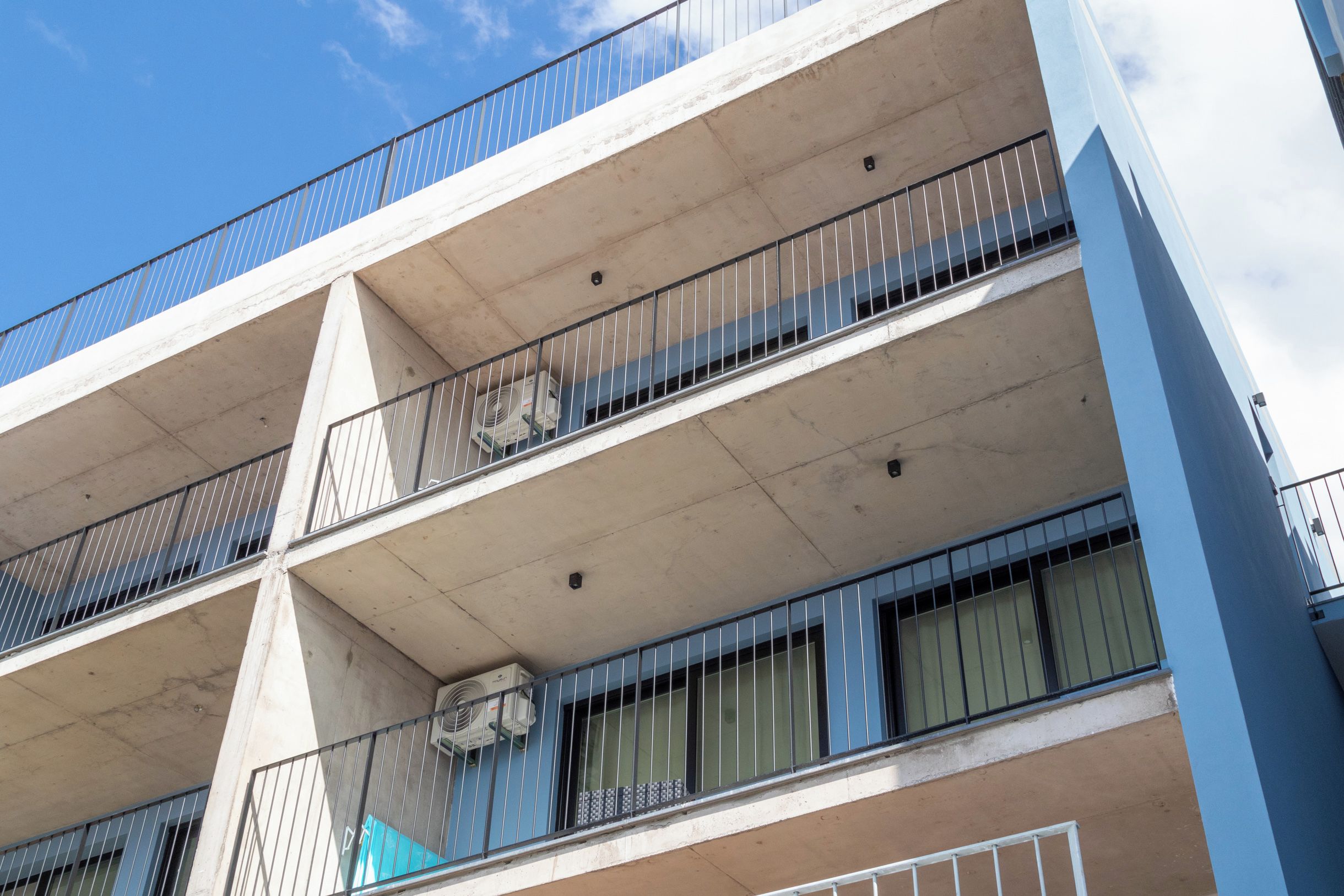 Un edificio de varios pisos con balcones, unidades de aire acondicionado y un cielo despejado.
