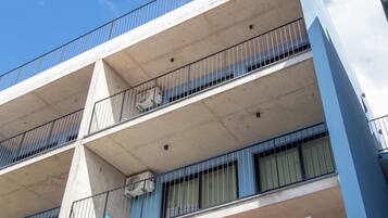 Un edificio de varios pisos con balcones, unidades de aire acondicionado y un cielo despejado.