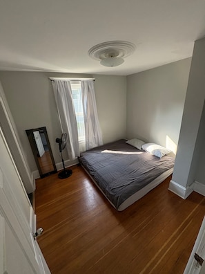 Een slaapkamer met een bed, een ventilator en een raam met gordijnen.