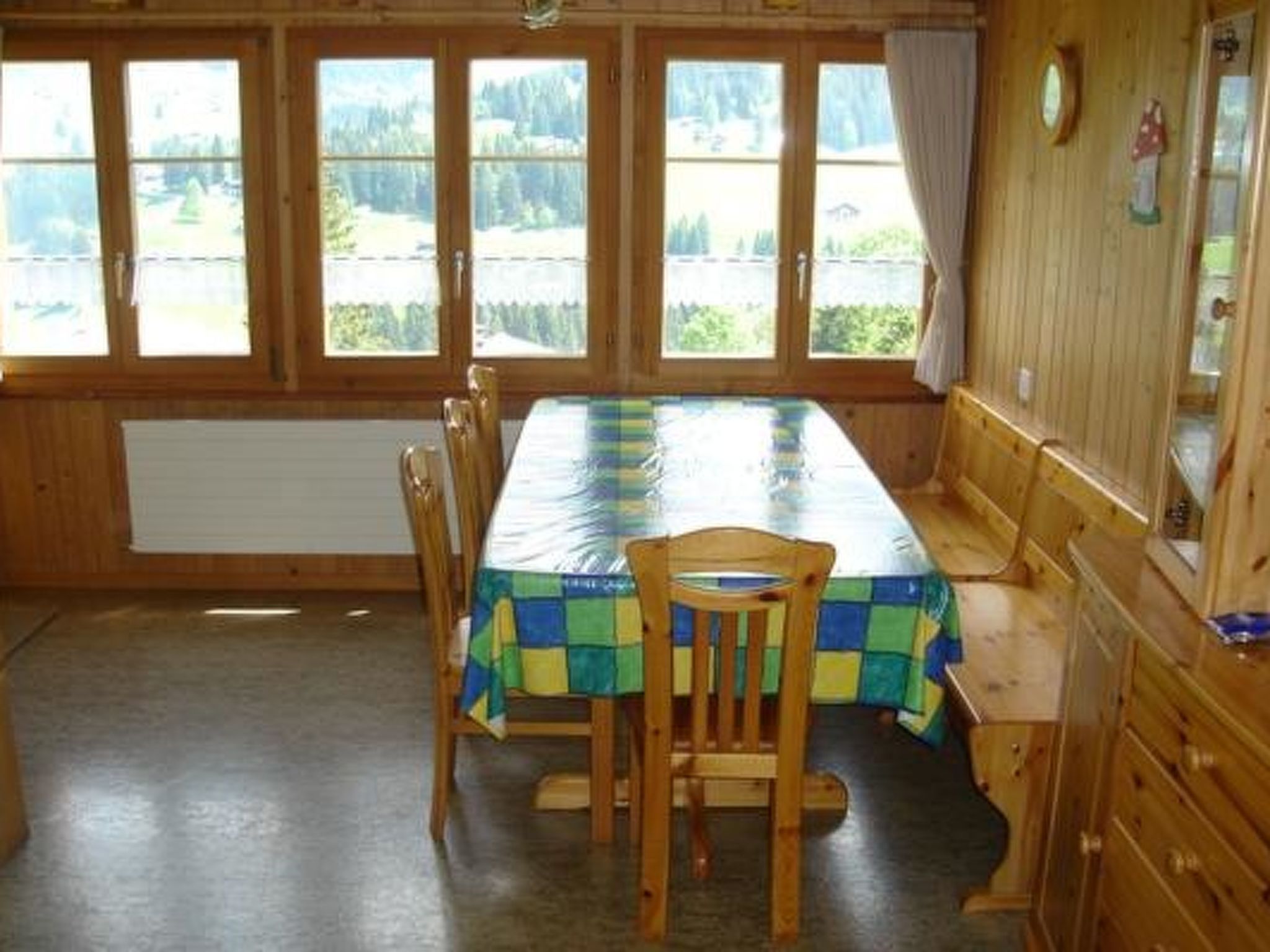 A dining area with a long table, chairs, and a view through large windows.
